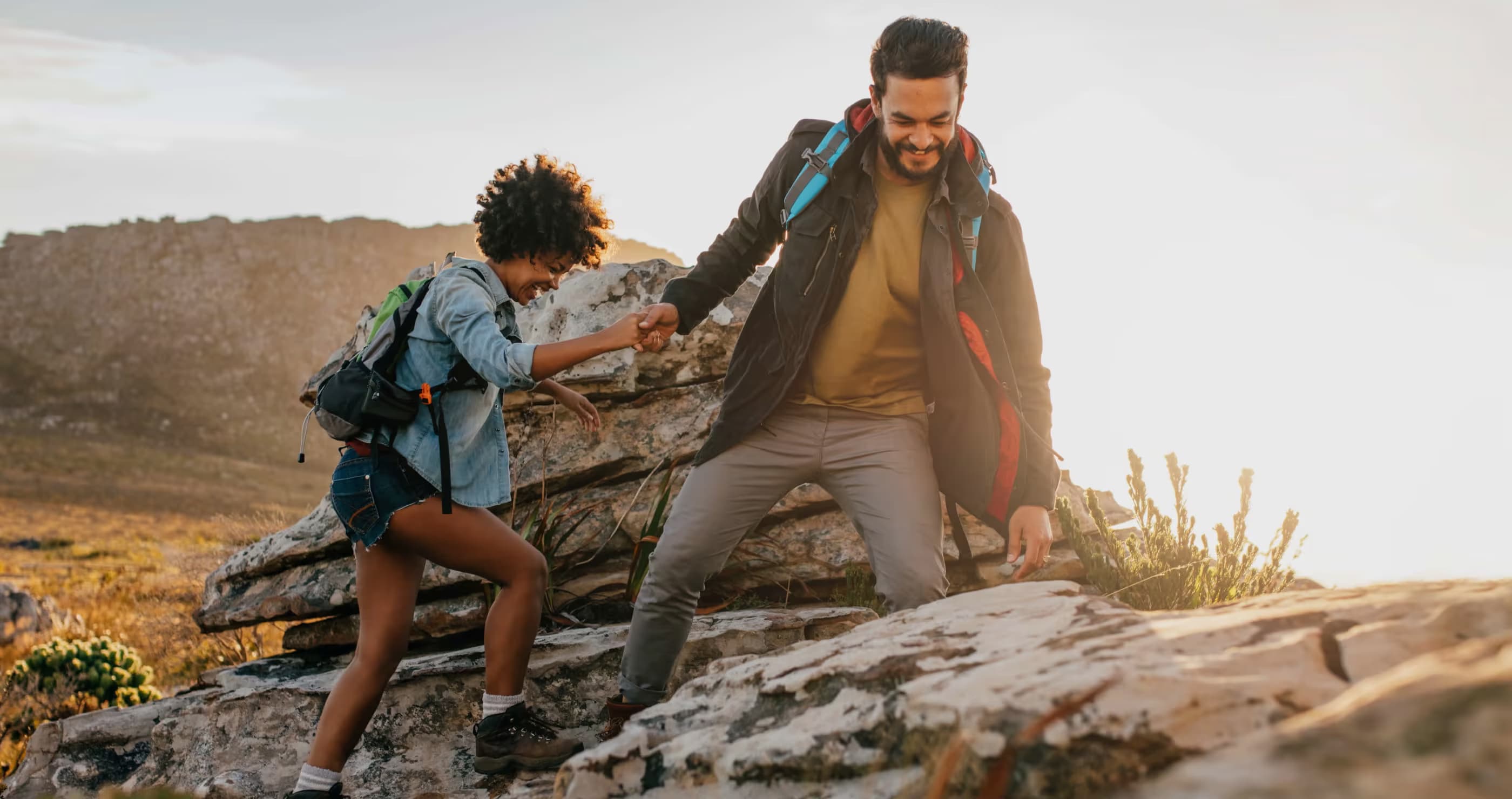 Two people hiking up rocky terrain while holding hands