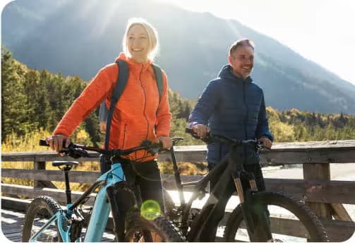 Two adults walking their mountain bikes over a small wooden bridge