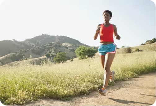 An adult running on a dirt track with a mountainous field in the background